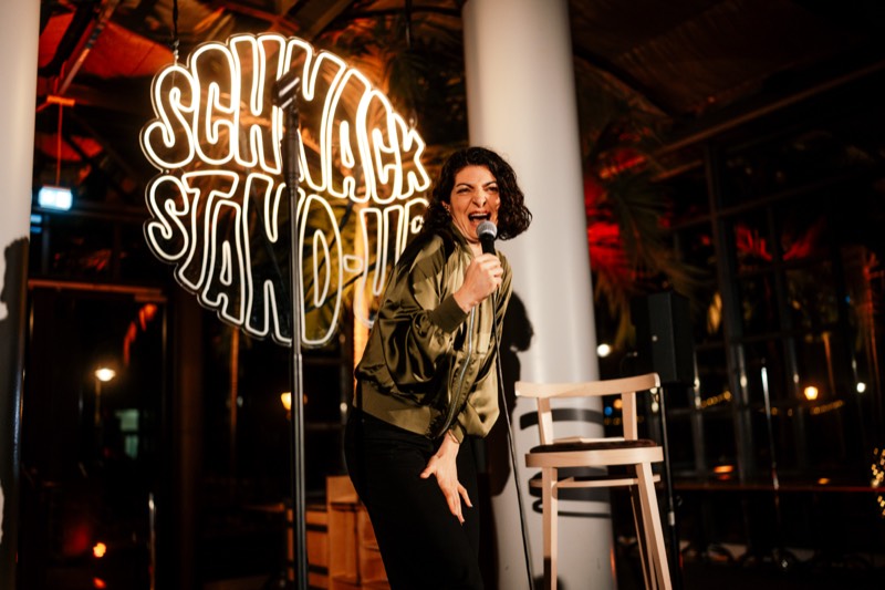 Comedienne in goldener Jacke vor dem SCHNACK Neonschild