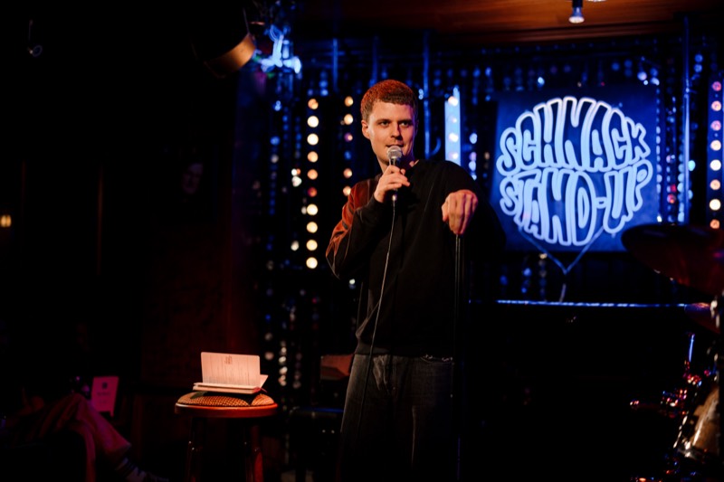 Comedian mit Mikrofon vor dem SCHNACK Stand-Up Neonschild